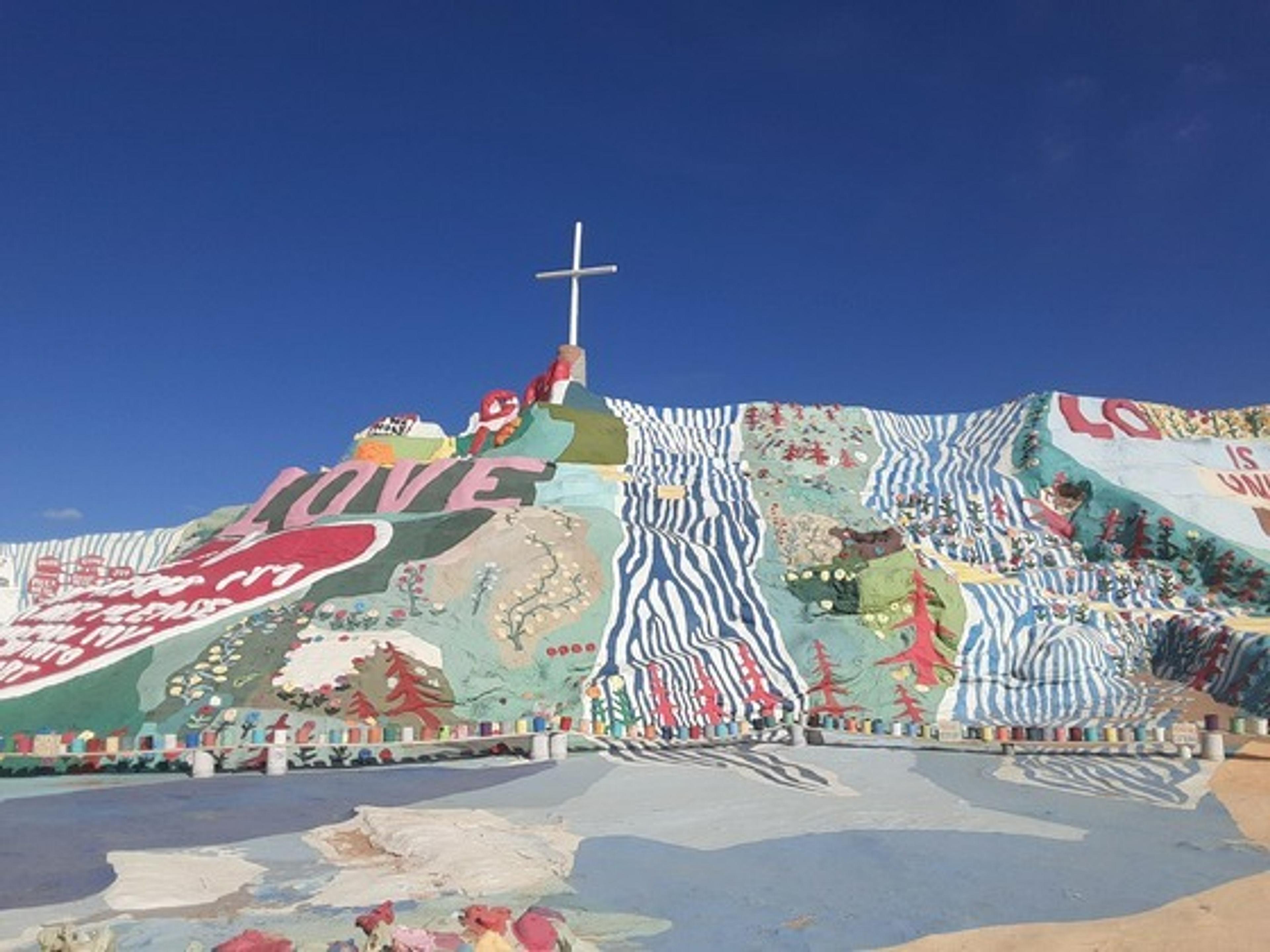 Hill covered with colourful murals, topped with a cross