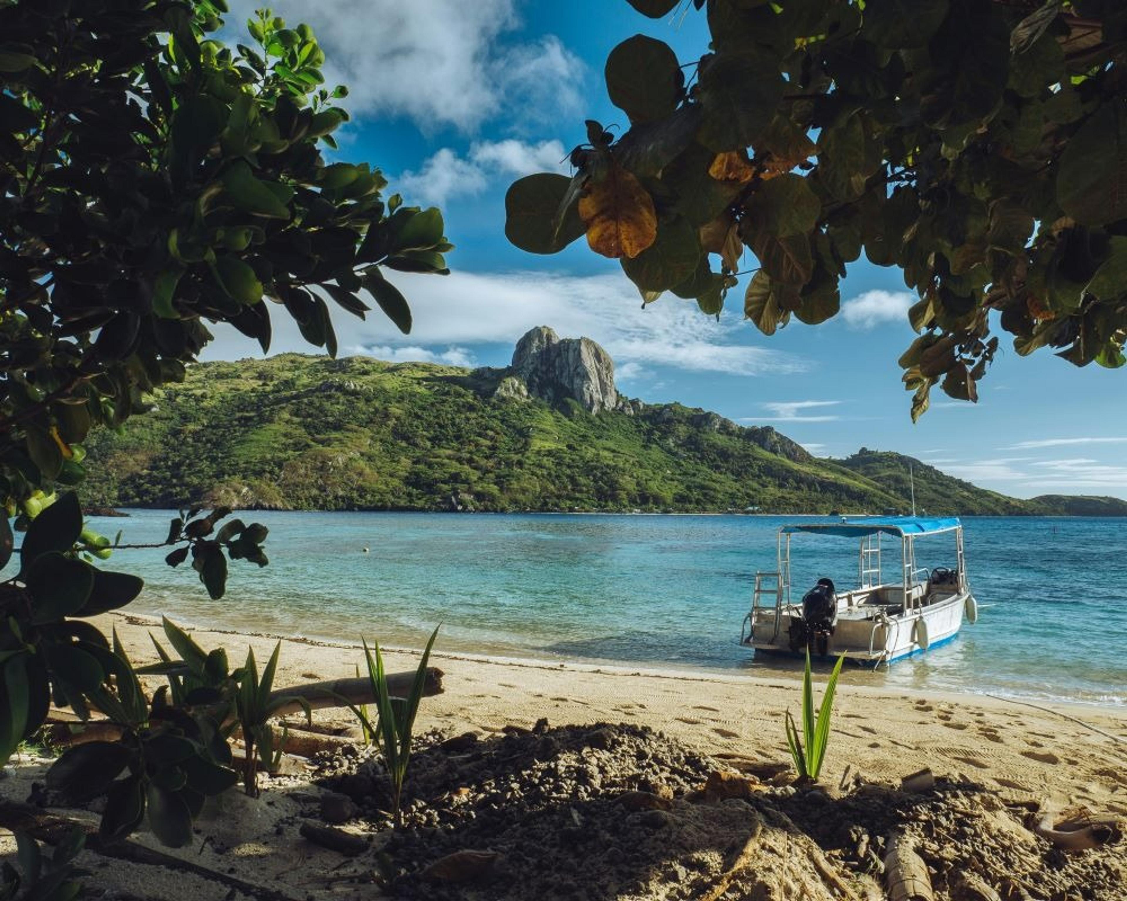 Secluded, leafy beach with a small boat floating by the shore, Fiji