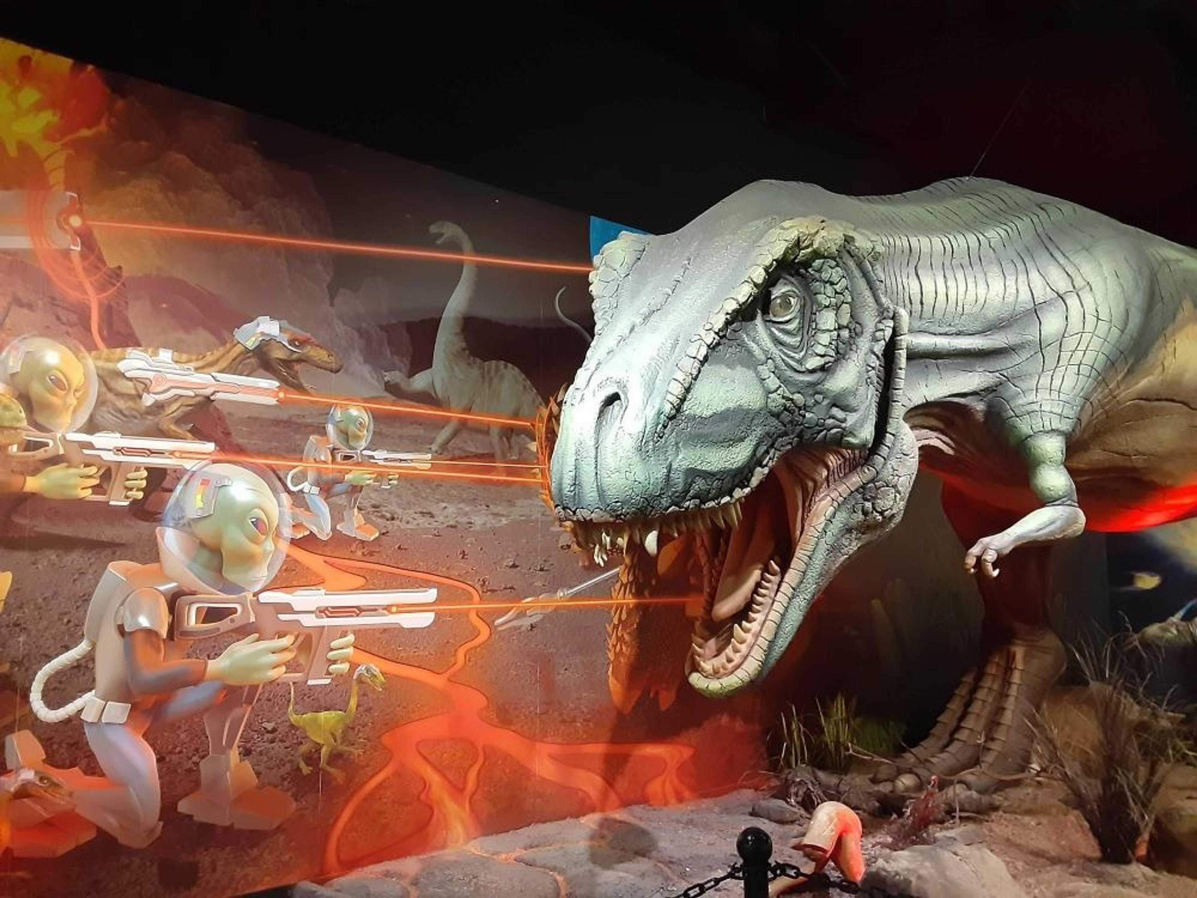 Huge T-Rex model in front of an image of aliens shooting towards it