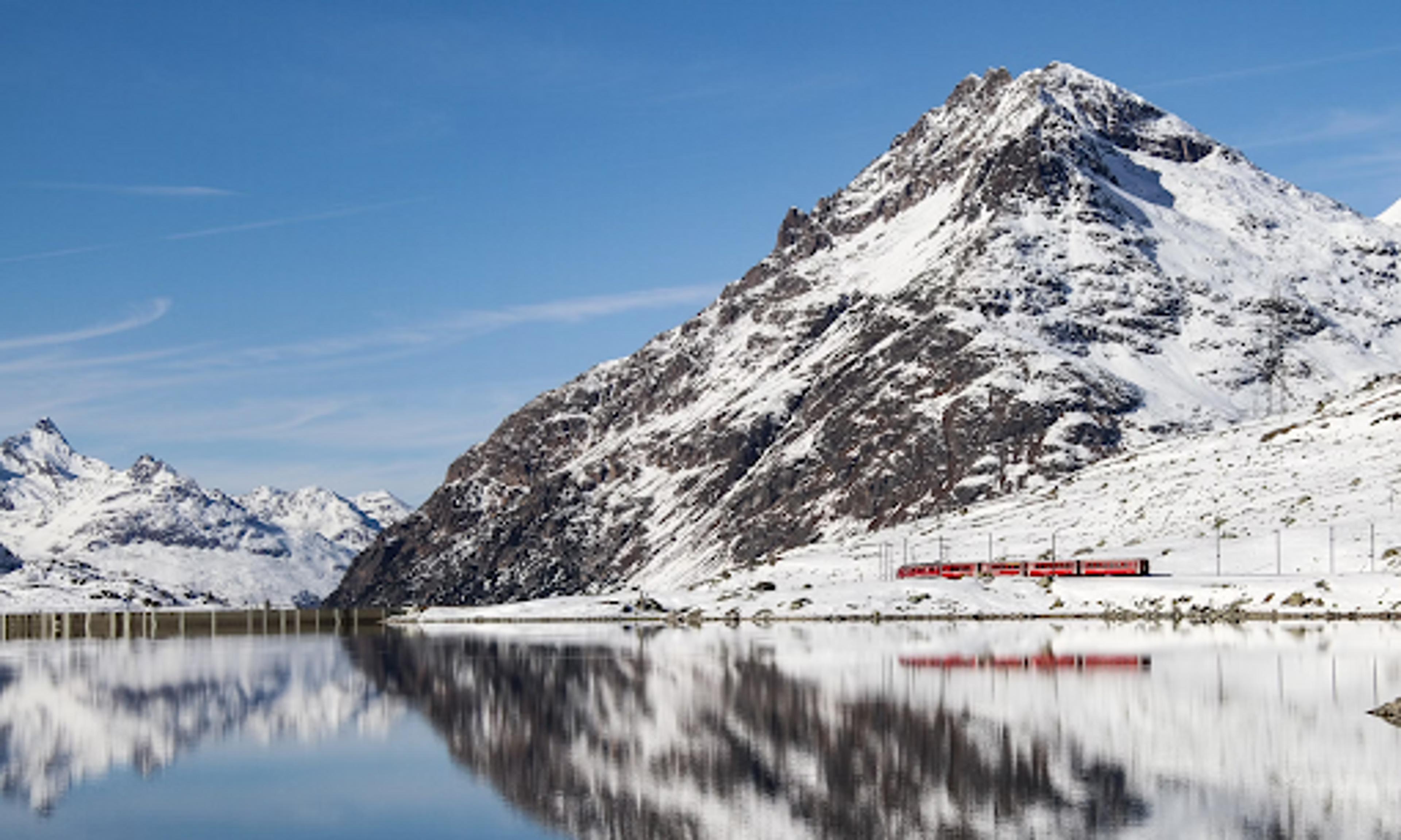 Red train passing snowy mountains