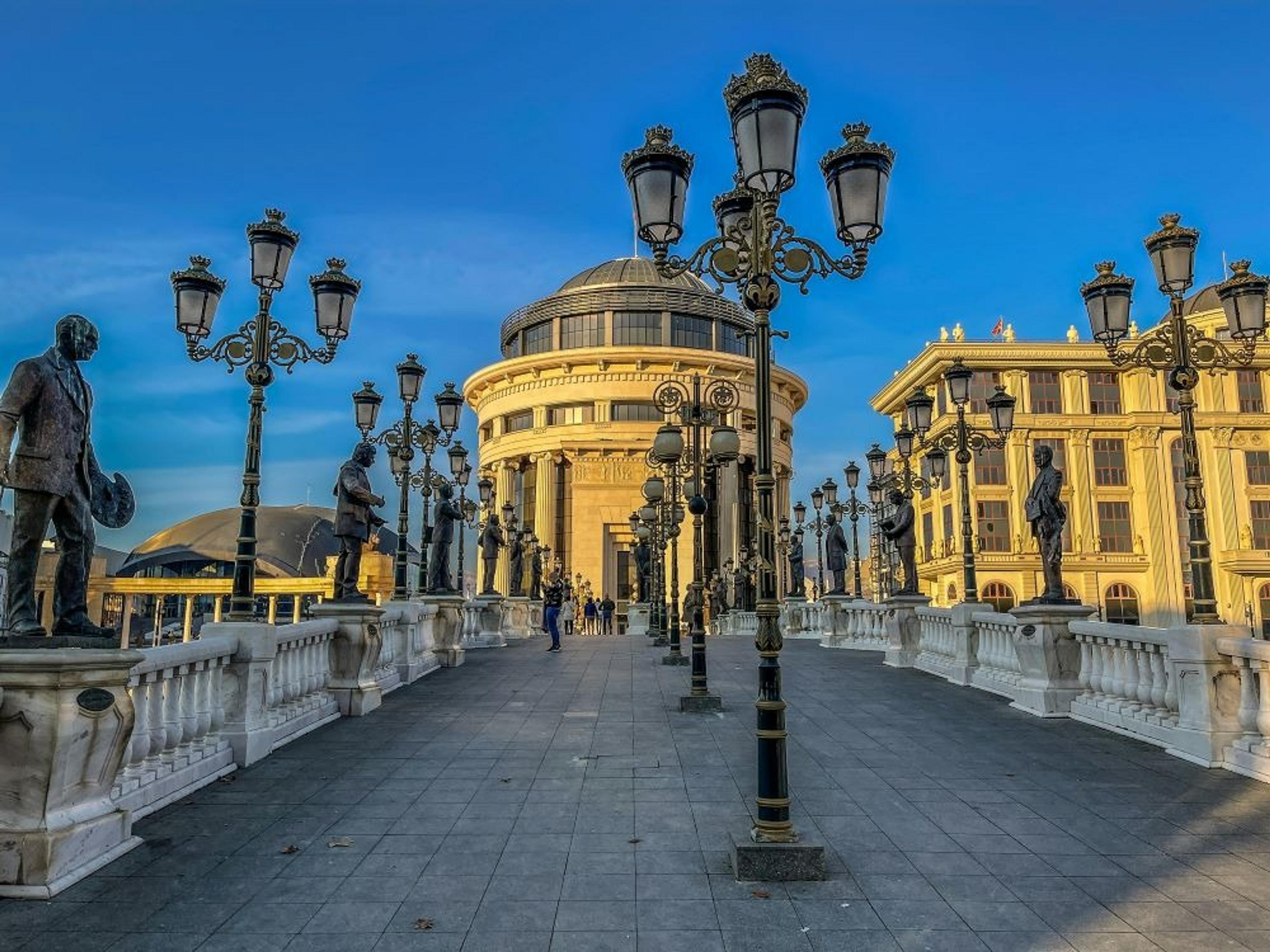 A bridge lined with ornate lamps leading to a yellow, domed building